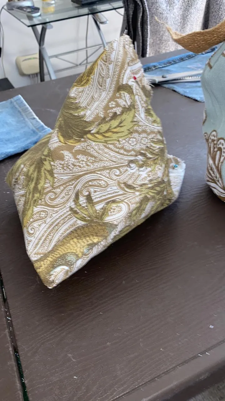 Cojín en pirámide con tela estampada en tonos verdes y dorados, sobre la mesa de costura