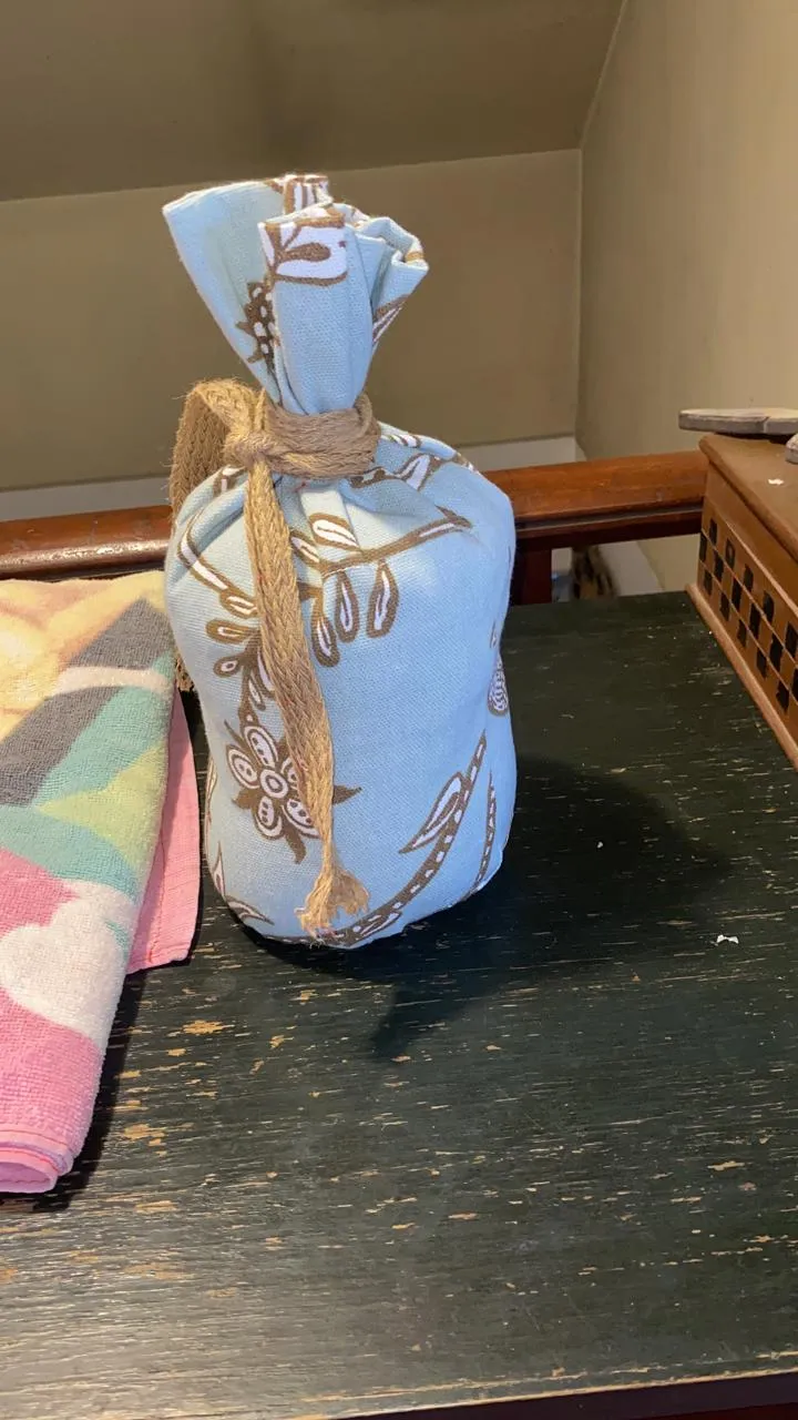 Tope de puerta hecho con una botella forrada en tela celeste estampada, amarrado con cordel